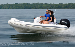 Lake boating in a GRAND golden line 11’10” long luxury fiberglass rigid inflatable boat (RIB) tender with steering console, seating, storage, bow step-plate, handrails, and outboard motor.